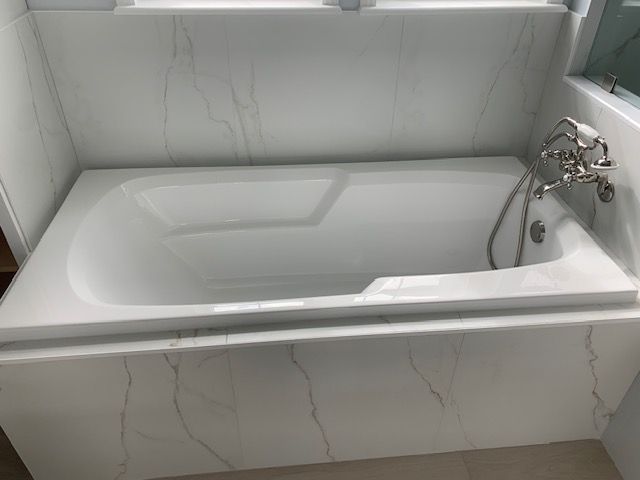 White bathtub in a modern bathroom with marble-look tile walls. Chrome faucet and showerhead.