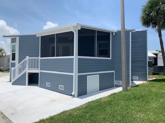 Small blue-gray house with white trim, screened porch, stairs, and a grassy yard under a clear sky