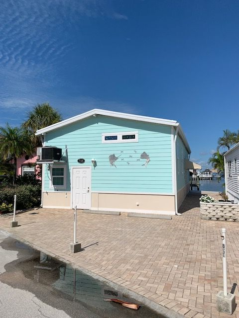 Pastel blue beach cottage with white doors and a palm tree under a clear sky