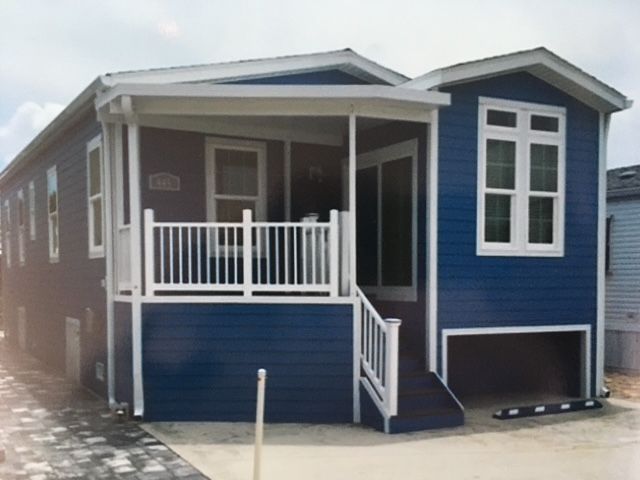 Blue modular home with a white porch and stairs, shown in an outdoor lot