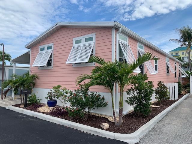 Pink coastal house with white shutters, palm trees, and tropical landscaping under a blue sky