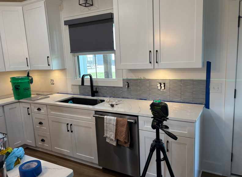 Bright white kitchen with cabinets, sink, window, and a camera on a tripod in the foreground