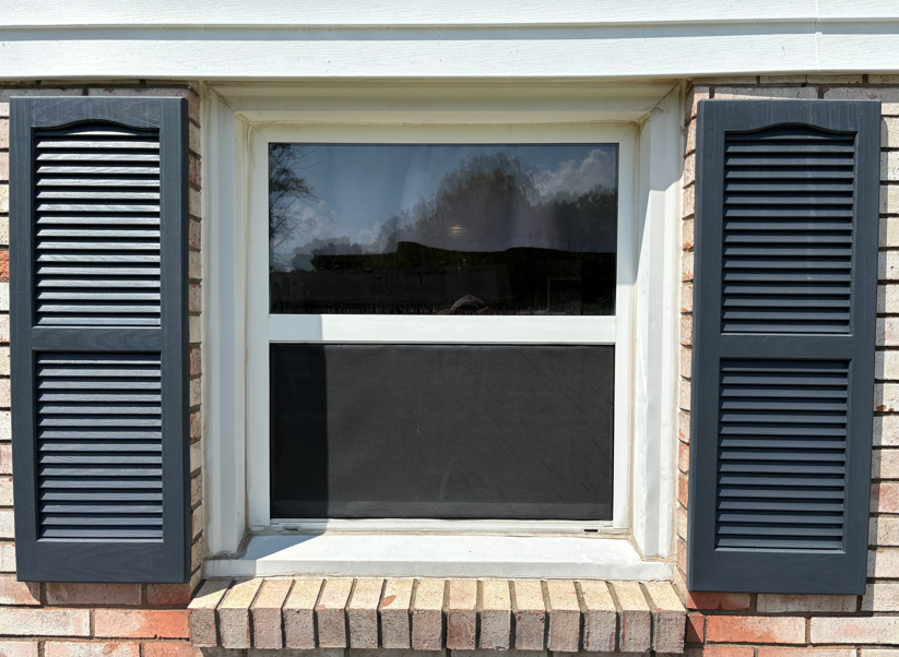 Closed window with dark shutters on a white house exterior