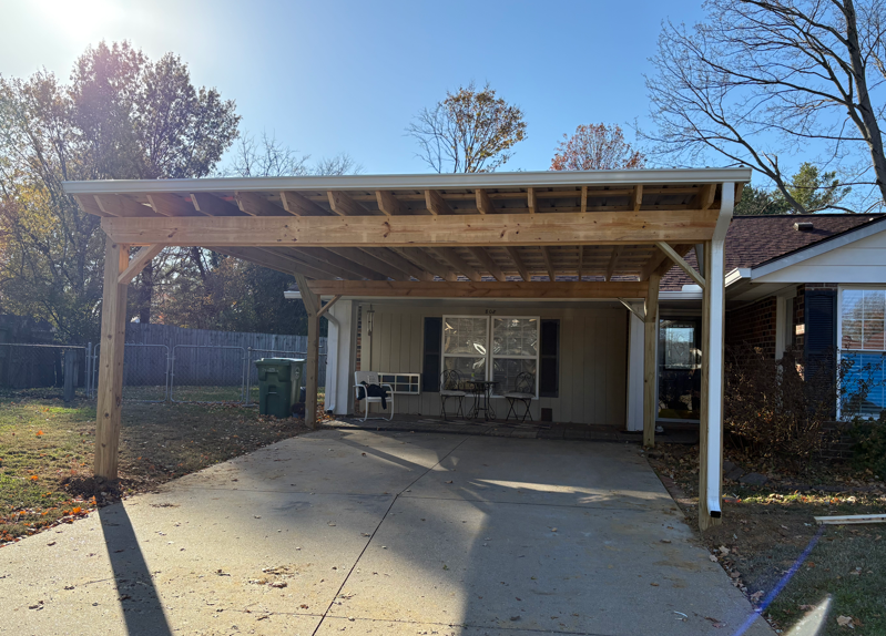 Front porch with a wooden pergola over a concrete driveway, leading to a house entrance.