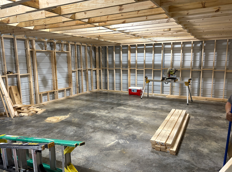 Interior of a partially built room with exposed wood framing, concrete floor, and construction tools on site