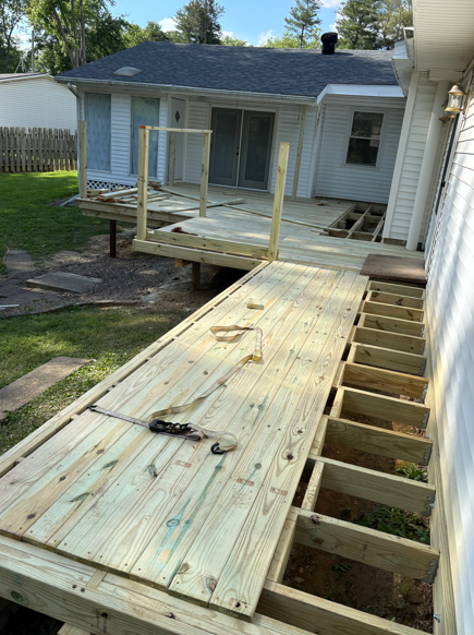 Partially built wooden ramp leading to a house deck, with exposed framing and handrails installed