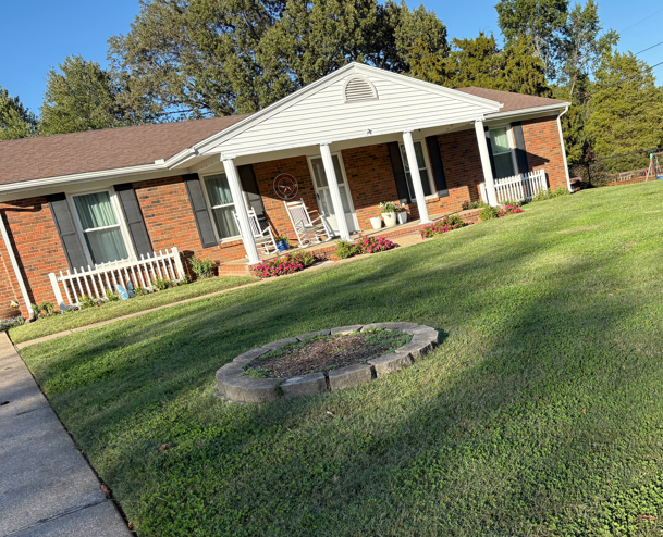 Brick house with white porch on a sloped lawn and circular fire pit in the foreground