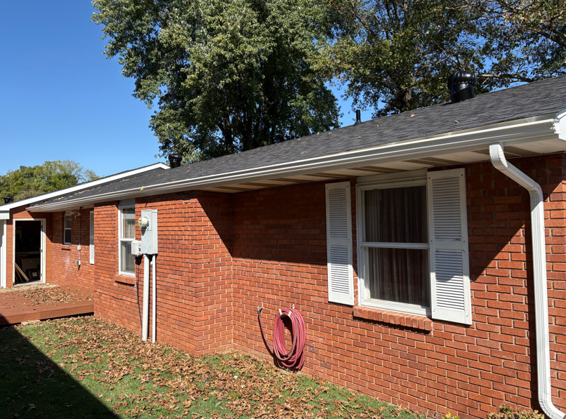 Brick house exterior with white shutters, utility meter, and red hose reel beneath a dark roof
