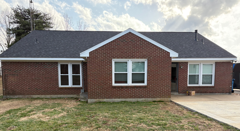Single-story red brick house with dark roof, white-trimmed windows, and a driveway on the right