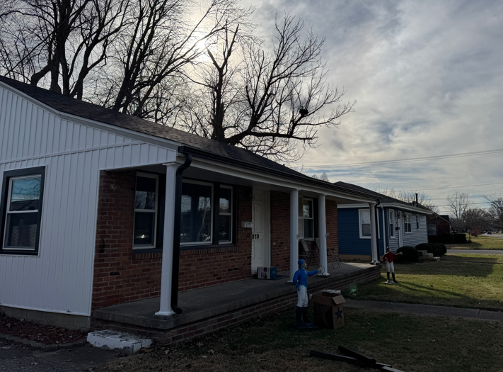 Single-story house with white siding and brick porch under a cloudy sky