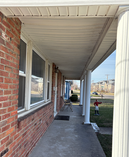 Brick house front porch with white columns, windows, and a child playing on the lawn in the distance