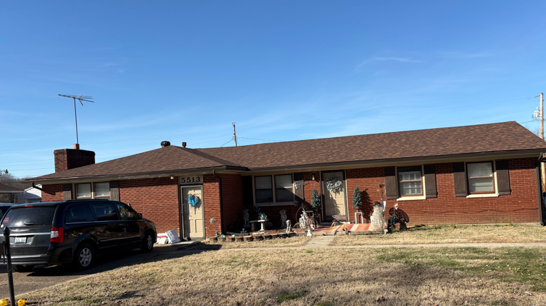 Single-story brick house with a black SUV parked in the driveway on a sunny day.