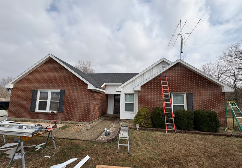 Brick house exterior with a red ladder, cloudy sky, and yard tools in front