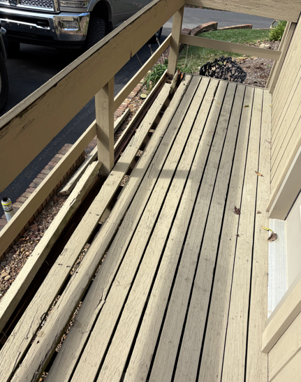 Narrow wooden porch or ramp with railings, stacked lumber, and a parked vehicle nearby.