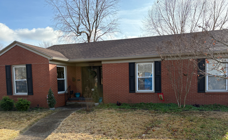 Single-story red brick house with a gray roof, blue shutters, and a small front porch.