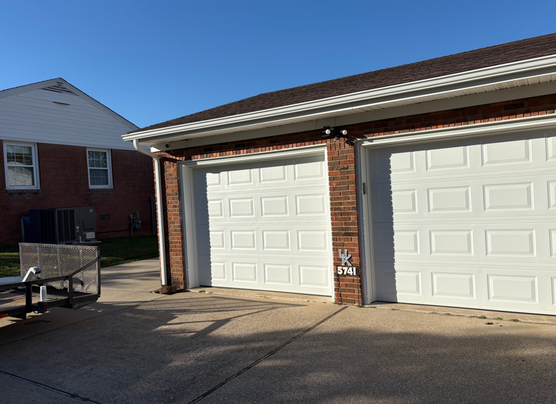 Two white garage doors on a brick house in bright sunlight