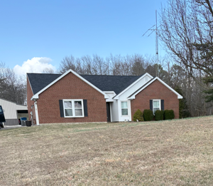 Single-story red brick house with white trim on a grassy lot under a clear blue sky