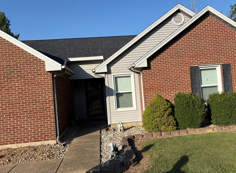 Brick suburban house with beige siding, dark roof, front walkway, and trimmed bushes
