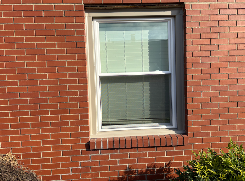 White-framed window in a red brick wall with closed blinds.