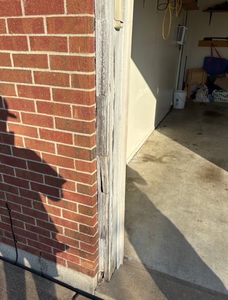 Open garage doorway beside a red brick wall, with sunlight casting shadows on the concrete floor.