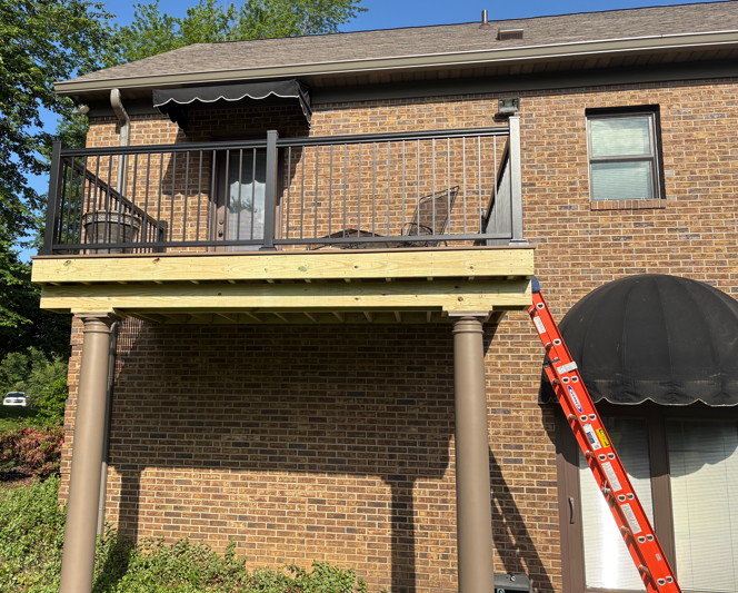 Brick house balcony with awning, black railing, and a red ladder leaning against it