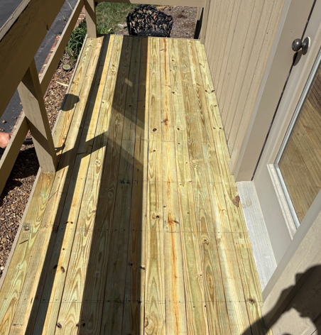 Wooden deck boards under construction on a narrow outdoor balcony beside a beige wall and sliding door