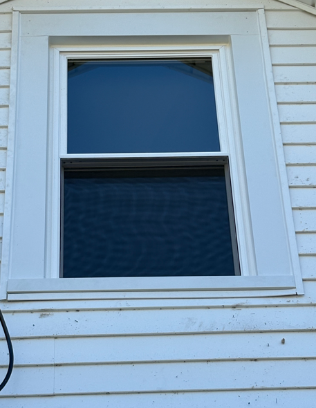 White house window with blinds and blue reflections, framed by white trim and siding.