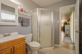 Small bathroom with sink, toilet, glass shower, and tan tile floor, viewed from the doorway
