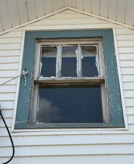 Old white house exterior with a blue-trimmed window and broken upper panes