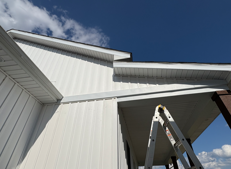 White house roof and siding with an open ladder beneath a blue sky