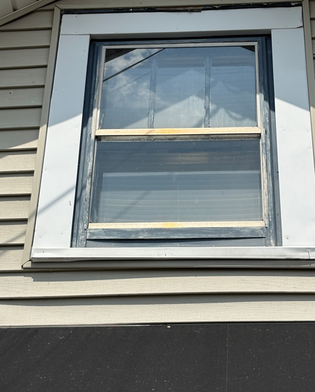 Close-up of a white-framed house window with a dark screen and beige siding outside.