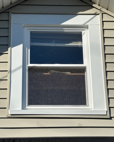 White-framed double-hung window on beige house siding in bright sunlight