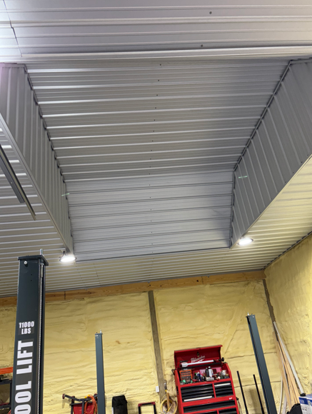 Warehouse ceiling with metal beams, a black support column, and a red ladder against a yellow wall