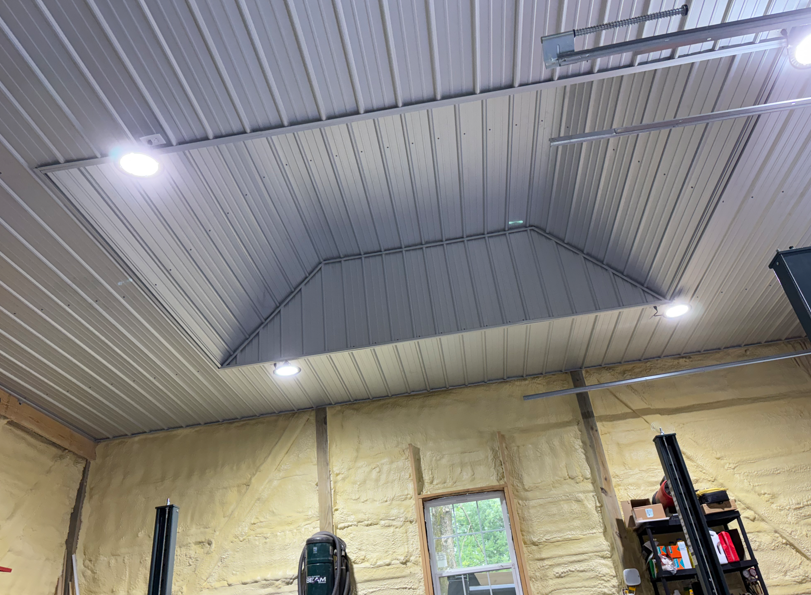 Warehouse interior with insulated metal ceiling, bright lights, and exposed wall insulation above shelves and equipment