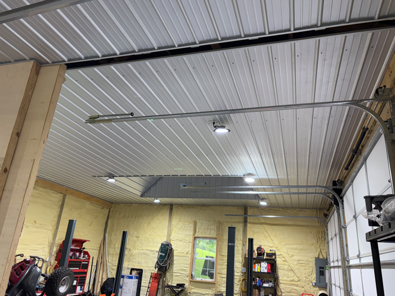 Workshop interior with high corrugated metal ceiling, skylights, yellow brick walls, and shelves of tools.