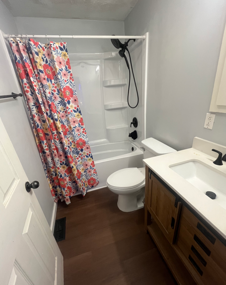 Small bathroom with floral shower curtain, white tub, toilet, and wood vanity with sink.