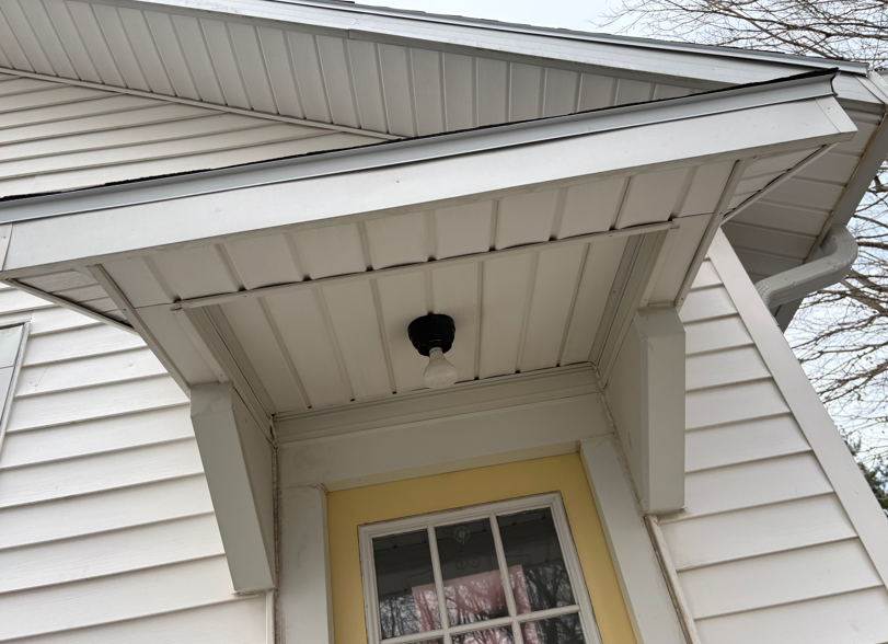 Front porch roof with white siding and a yellow-trimmed window beneath it