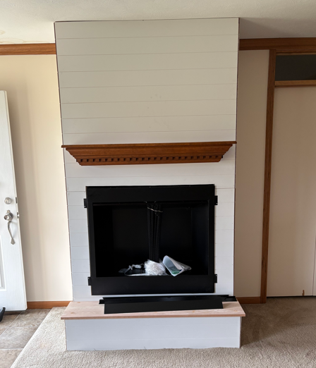 Living room fireplace with white mantel, black firebox, and light wood trim built into the wall