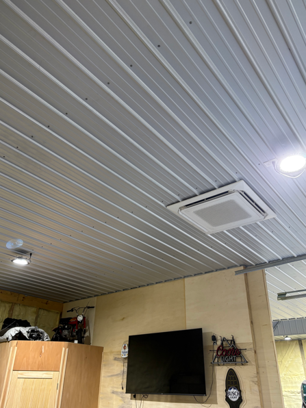 Ceiling with recessed lights and vents above a room with a TV and wooden cabinet