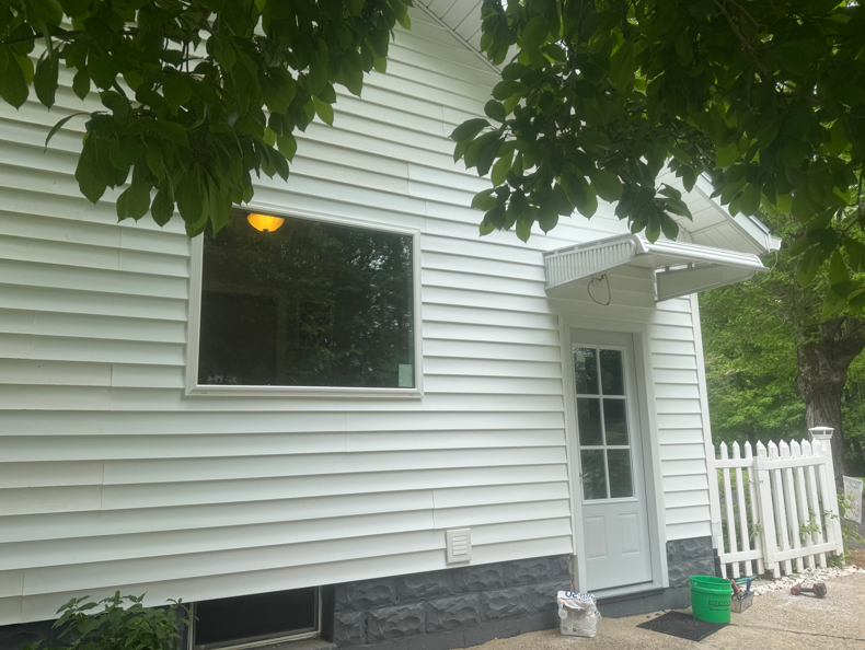 White house exterior with a side door, window, white fence, and trees in the yard