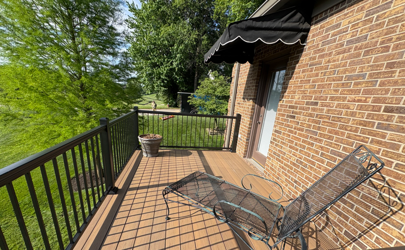 Brick house deck with black railings, metal chair, and a potted plant in bright sunlight