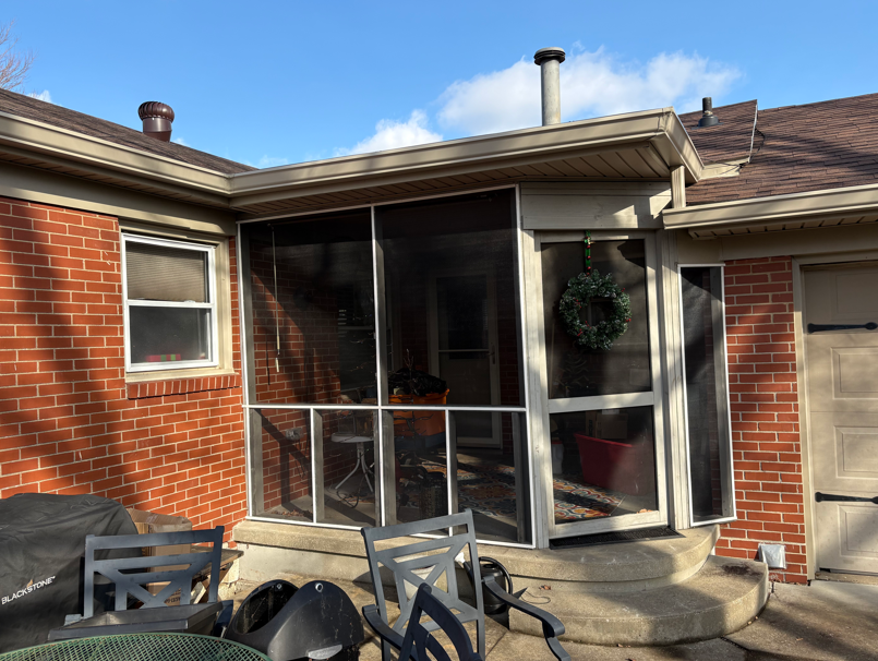 Brick patio with screened porch, outdoor chairs, and a hanging plant beneath a blue sky
