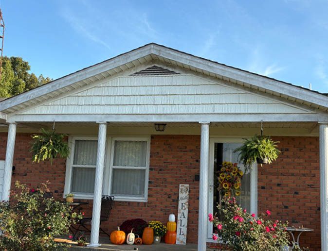 Brick house front porch decorated with Halloween pumpkins, flowers, and white columns under a gabled roof