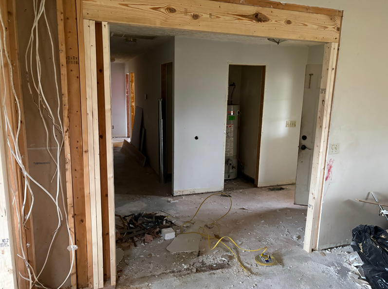 Partially demolished interior room with exposed framing, debris on the floor, and doorways to adjoining spaces