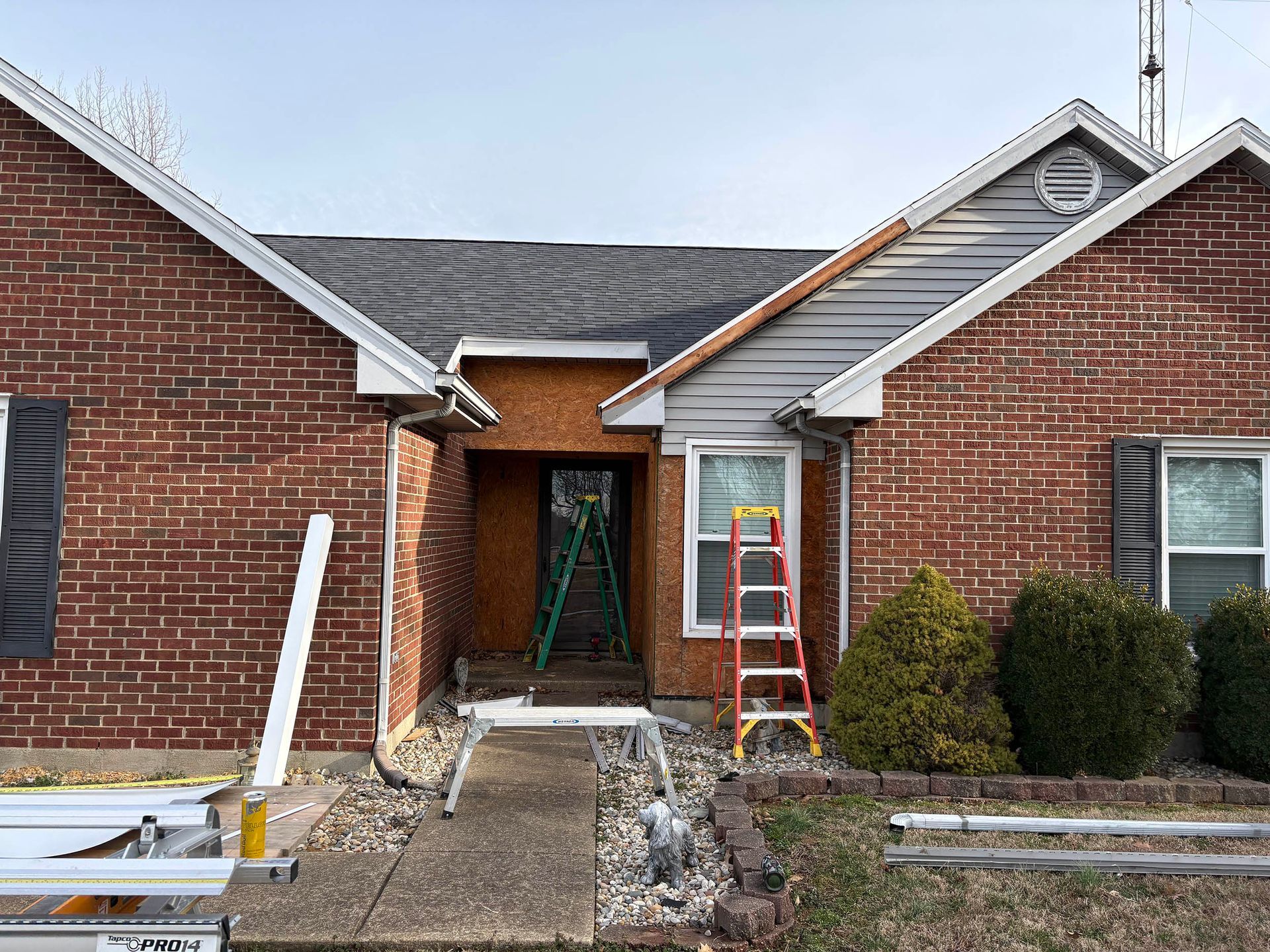 Brick house entry under repair, with ladders, tools, and a partially finished walkway.