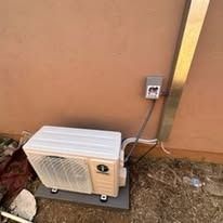 Outdoor air conditioning unit with electrical outlet and tube mounted on a brown wall.