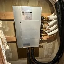 Silver control panel with copper pipes and black tubing mounted on a wall.