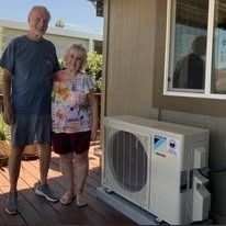 Man and woman posing by air conditioning unit on deck; smiling.