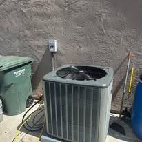 Air conditioner unit next to trash cans and a building in the sun.