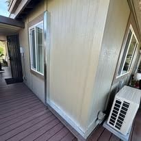 Corner of a house with a window and air conditioner unit on a wooden deck.